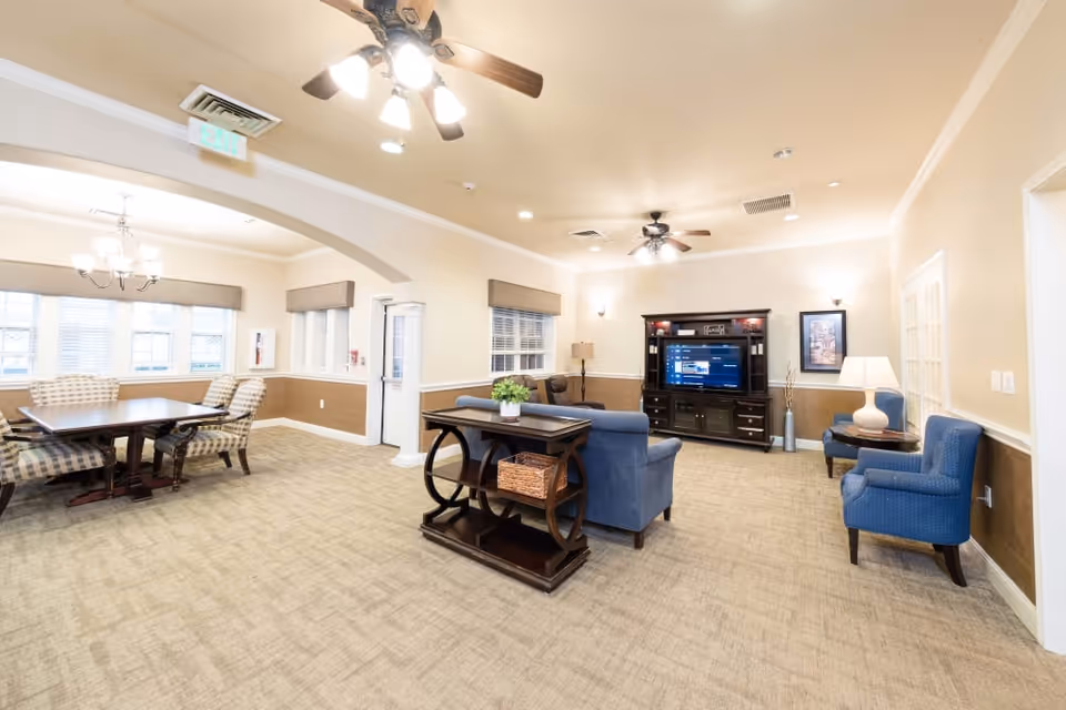 A spacious, well-lit communal living room with sofas, armchairs, an entertainment center, and a dining table.