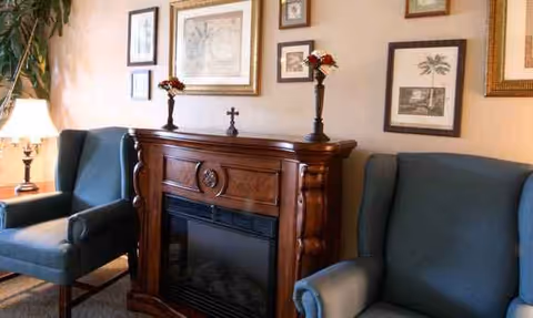Cozy living room area with blue chairs, a wooden fireplace, and framed wall art.