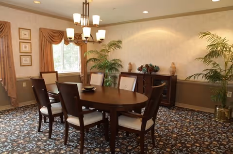 Formal dining room with an oval wooden table surrounded by six chairs, a chandelier overhead, a sideboard, and potted plants.