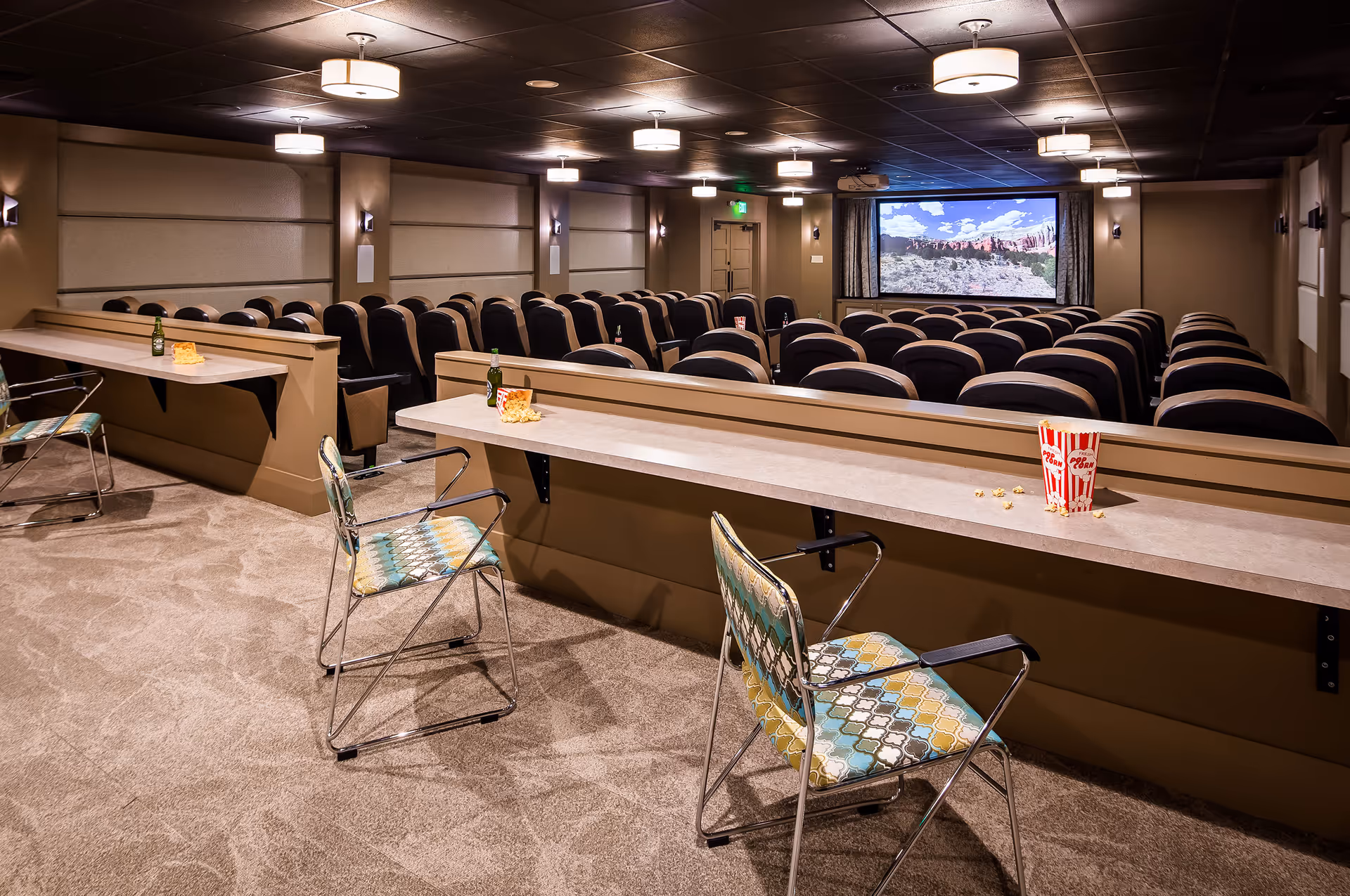 A cozy theater-style screening room with rows of seats, a large screen at the front, and counter seating with chairs and popcorn.