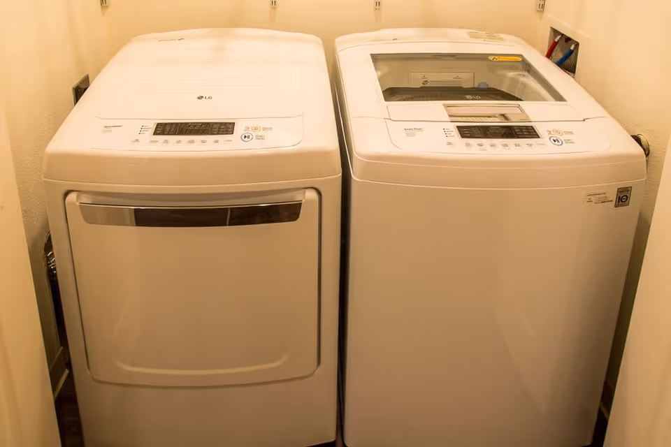 A laundry area with a white LG front-loading dryer on the left and a white LG top-loading washing machine on the right, placed side by side against a beige wall.