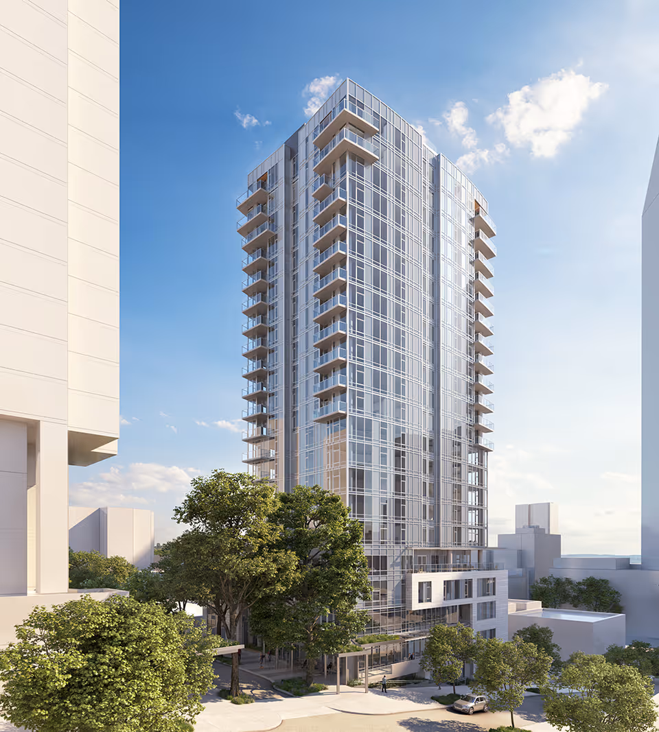 A modern glass high-rise residential tower with balconies rising above trees and low-rise buildings under a clear blue sky.