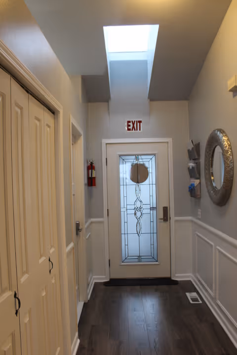 Interior hallway leading to a decorative glass exit door with a skylight overhead, closets on the left and a mirror on the right.