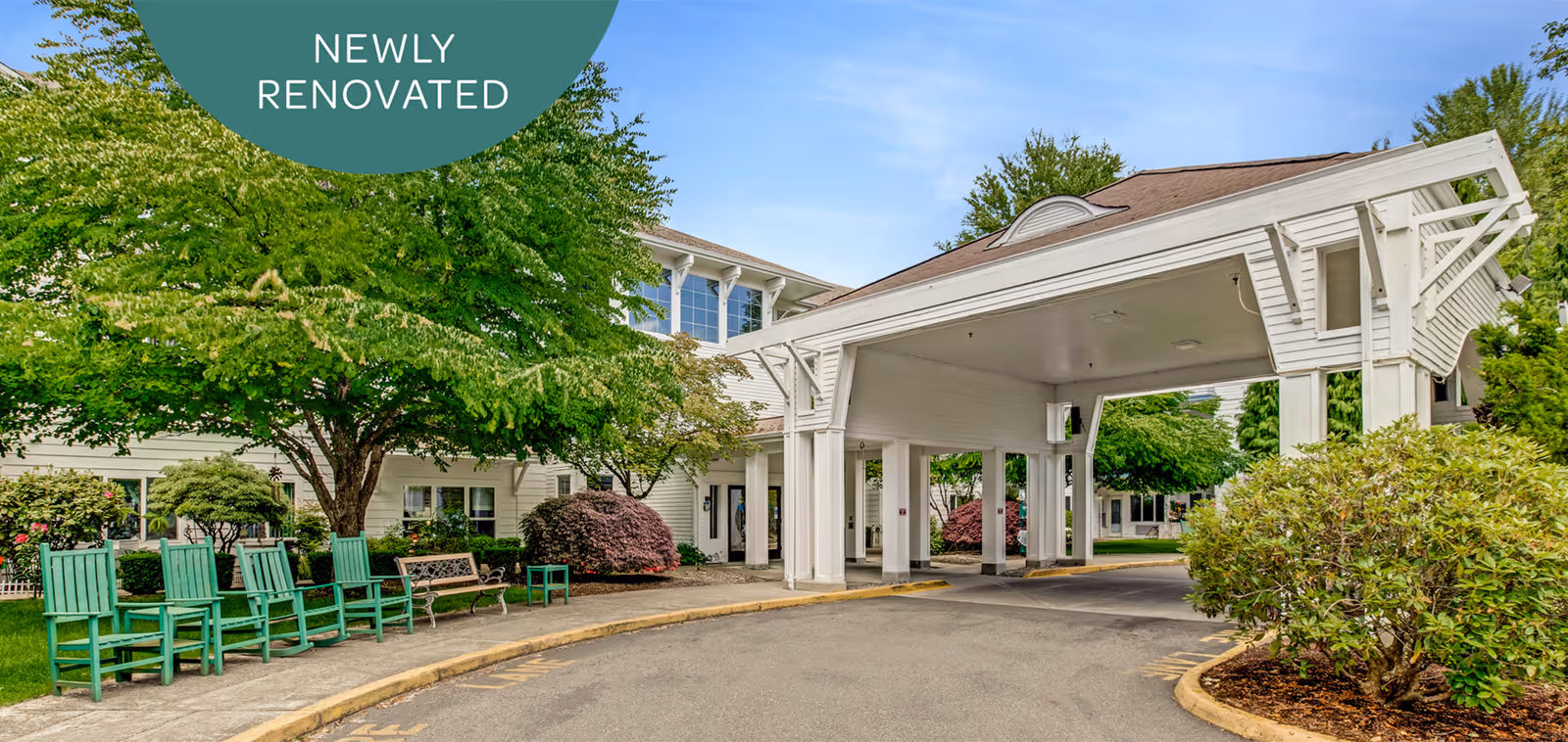 Exterior view of a senior living facility named Holiday South Hill showing a covered driveway entrance with white pillars and a brown roof. There are green trees, bushes, and several green chairs and benches along the sidewalk. A green banner in the top left corner reads 'NEWLY RENOVATED'.