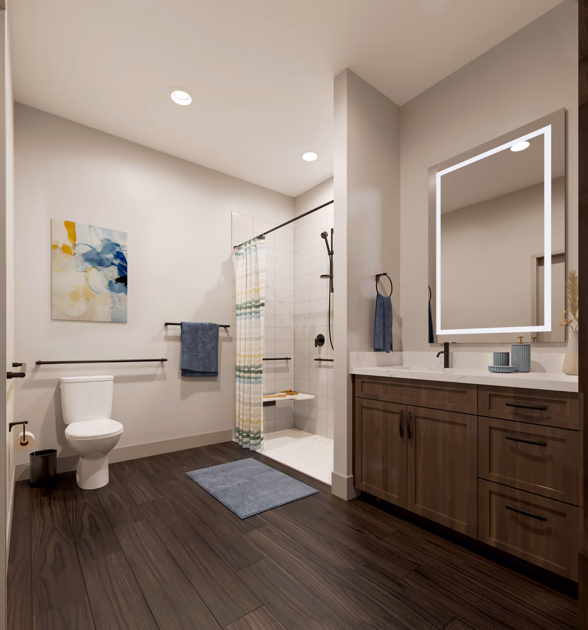 A modern bathroom with dark wood flooring, a white toilet, a walk-in shower with a striped shower curtain, and a wooden vanity with a white countertop and an illuminated rectangular mirror. There are blue towels hanging on black towel bars and a colorful abstract painting on the wall.