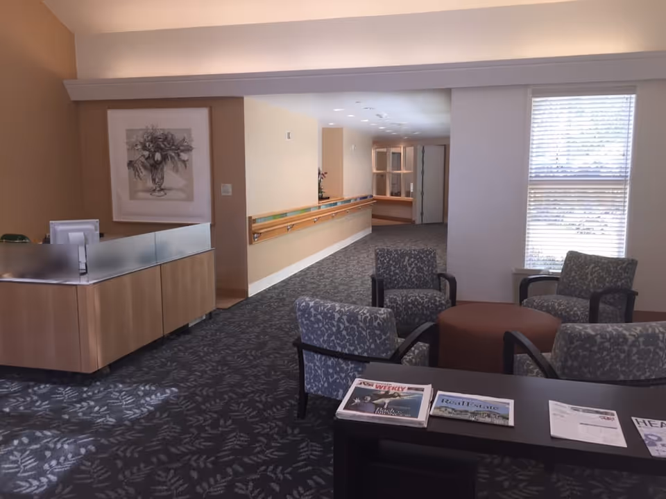 Lobby seating area with patterned chairs around a small table, a reception desk to the left, and a corridor leading further into the facility.