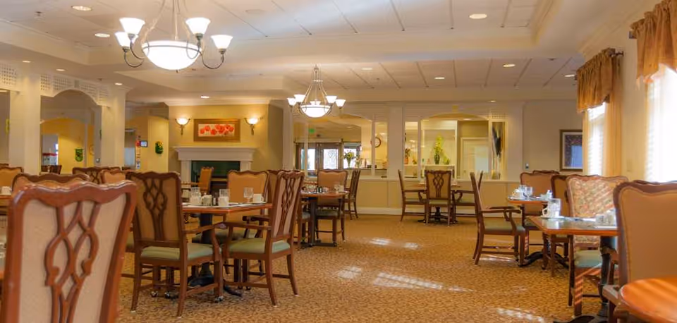 Spacious dining room with multiple set tables and upholstered chairs, chandeliers, and a fireplace.