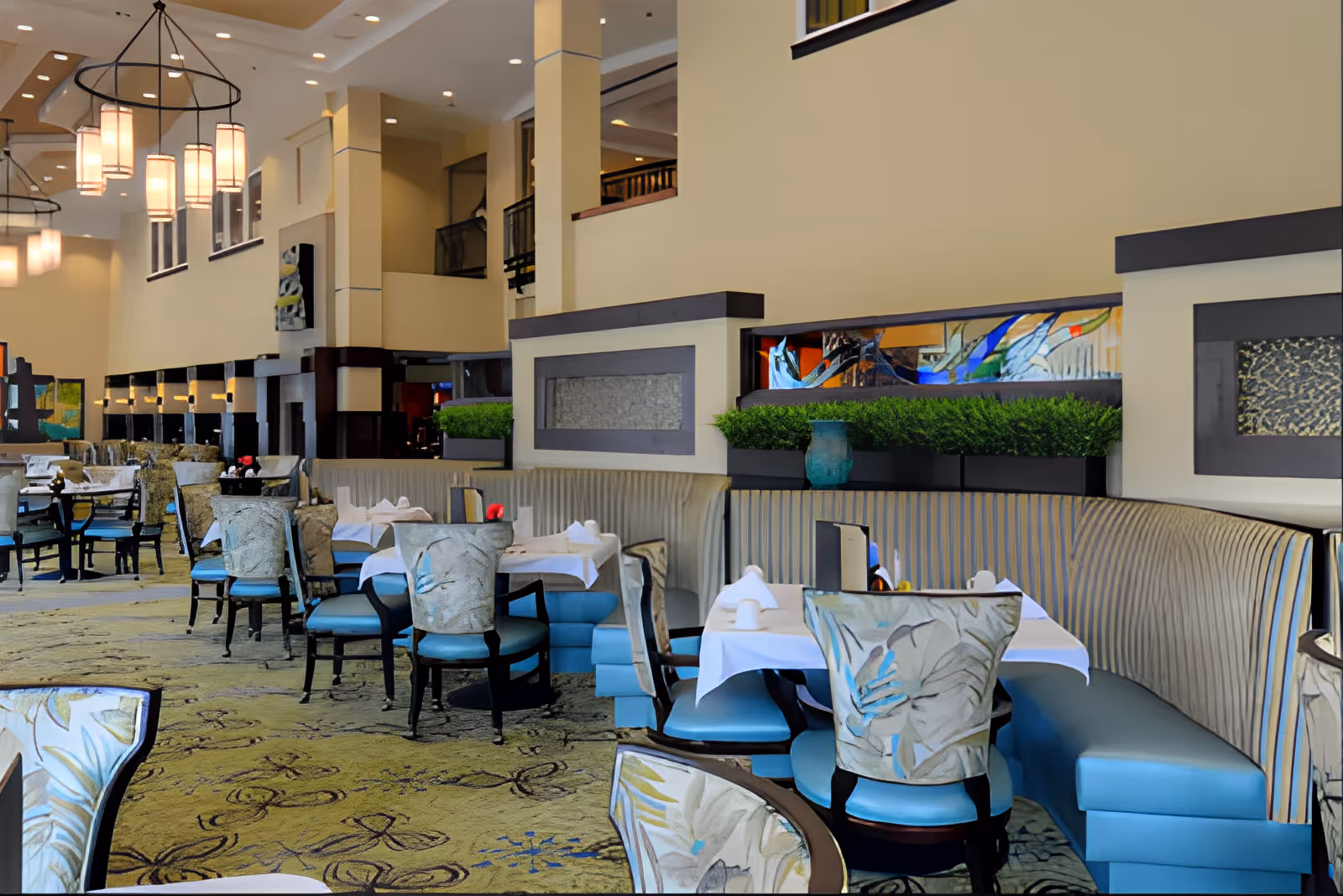 Spacious dining room with tables set for service, upholstered chairs and banquette seating under hanging pendant lights.