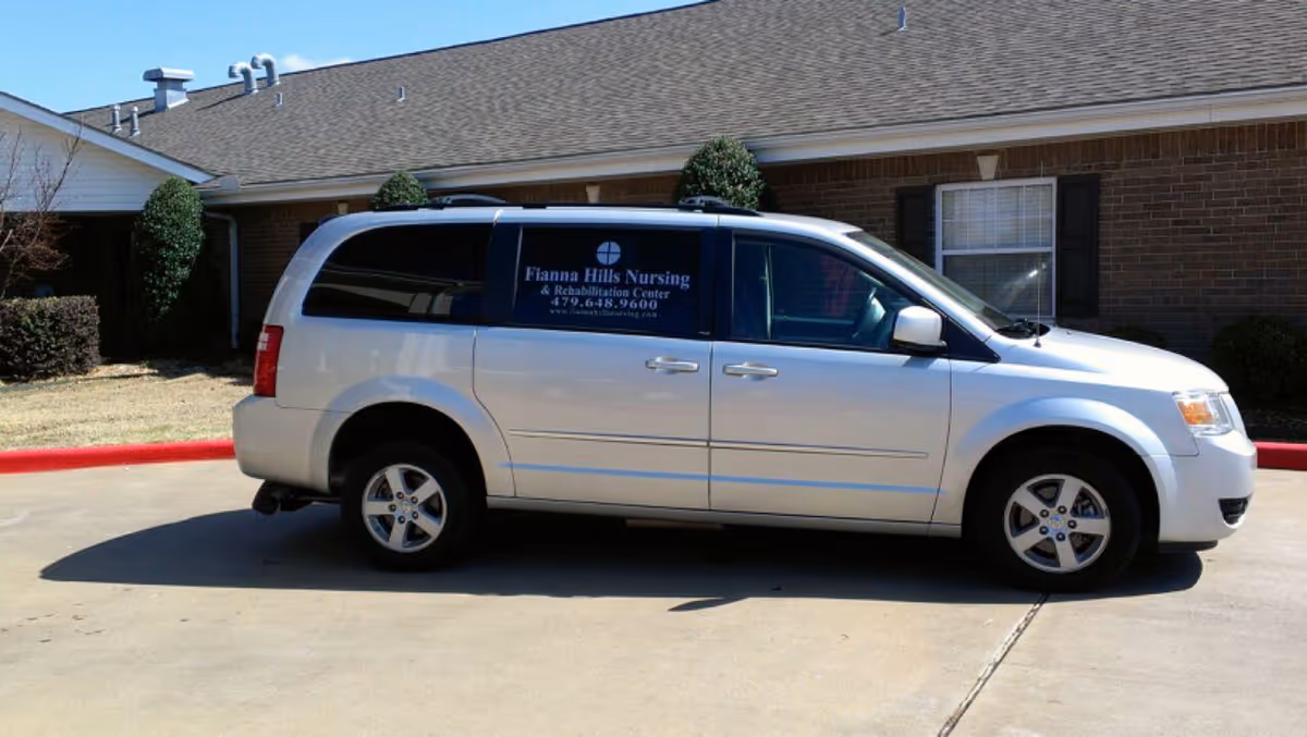 A silver shuttle van with 'Fianna Hills Nursing & Rehabilitation' signage parked in front of a brick nursing facility.