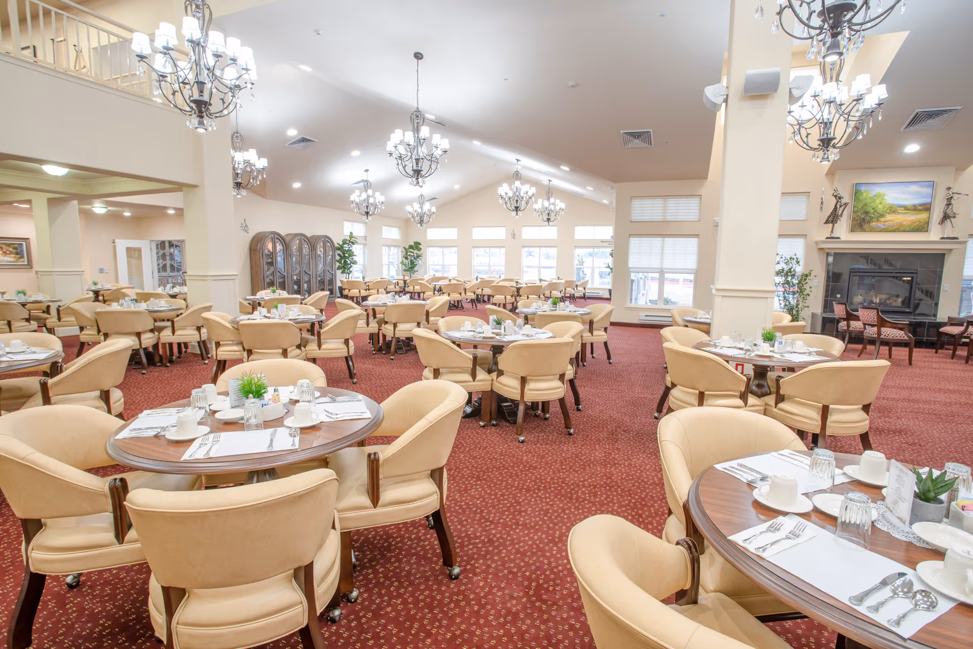 Spacious formal dining room with round tables and beige chairs set for meals in a senior living facility.