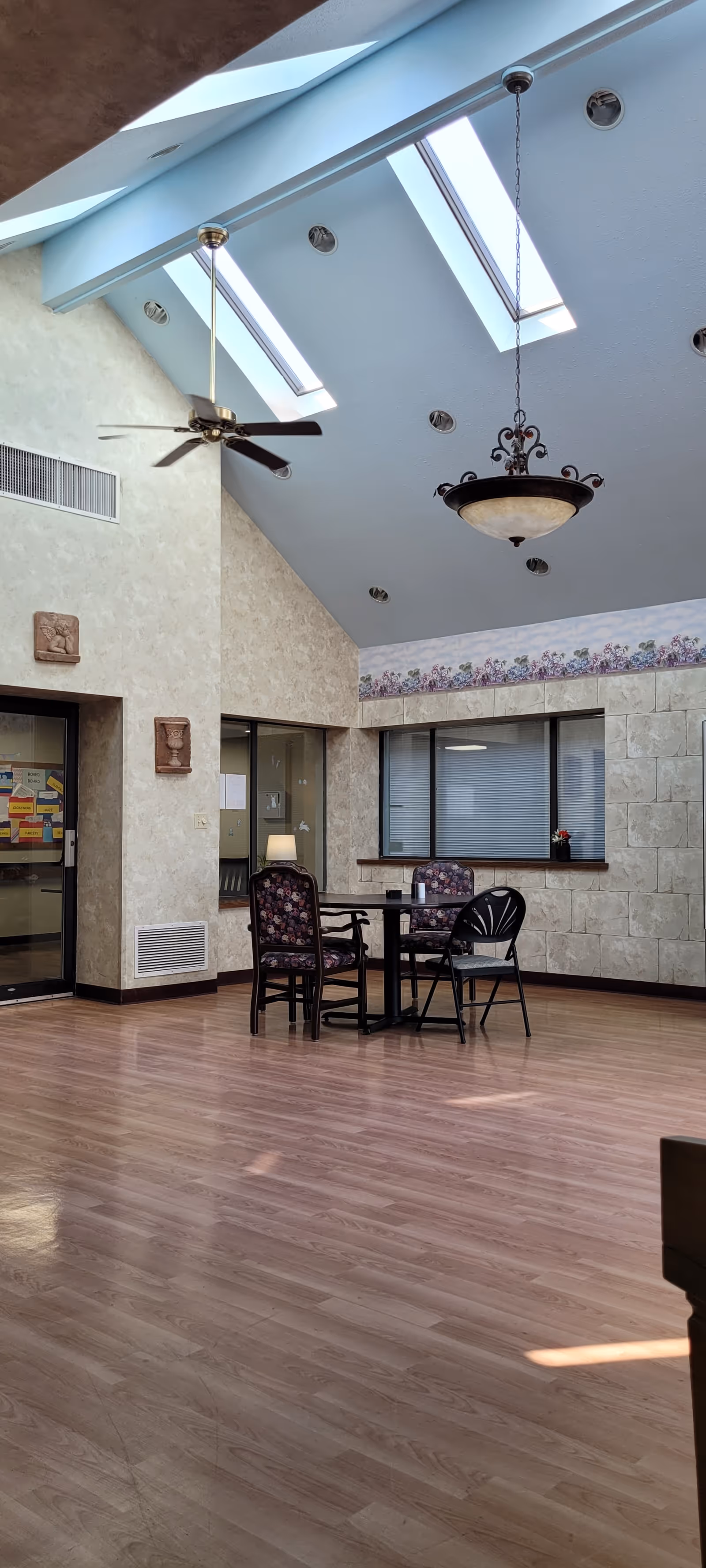 High-ceilinged interior common area with skylights, hanging lights, and a small table and chairs on a wood floor.