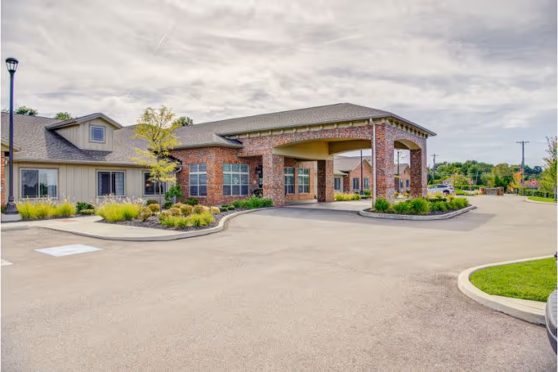 Covered entrance and porte-cochère of a brick memory care community building with landscaped beds and a circular driveway.
