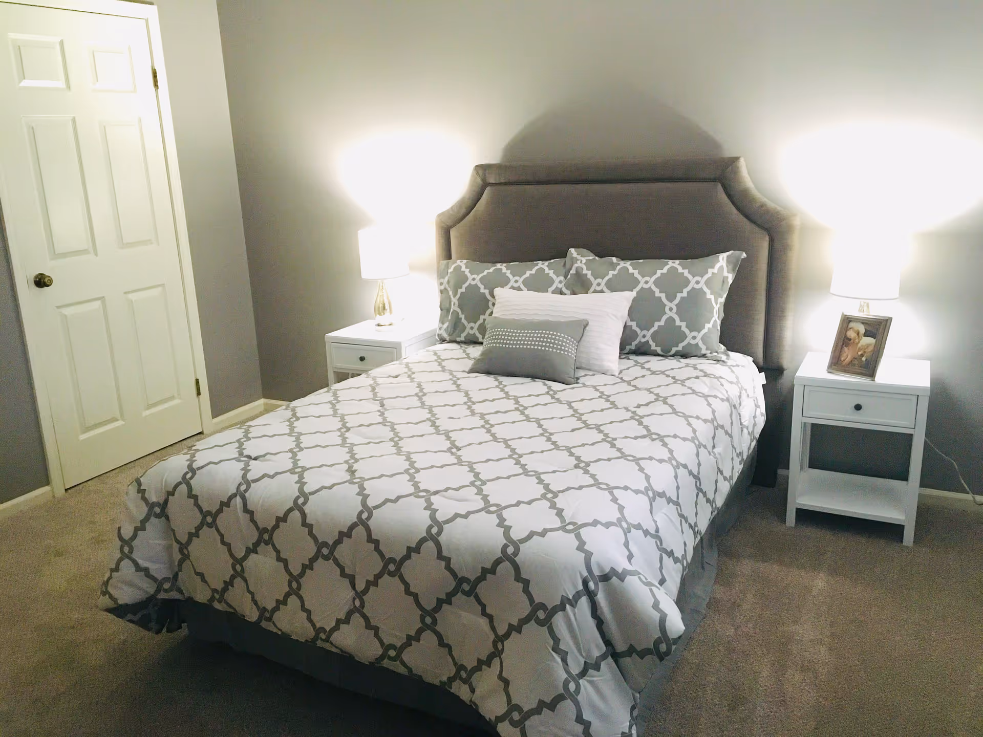 A neatly made bed with patterned bedding, upholstered headboard, and two nightstands with lamps in a softly lit bedroom.
