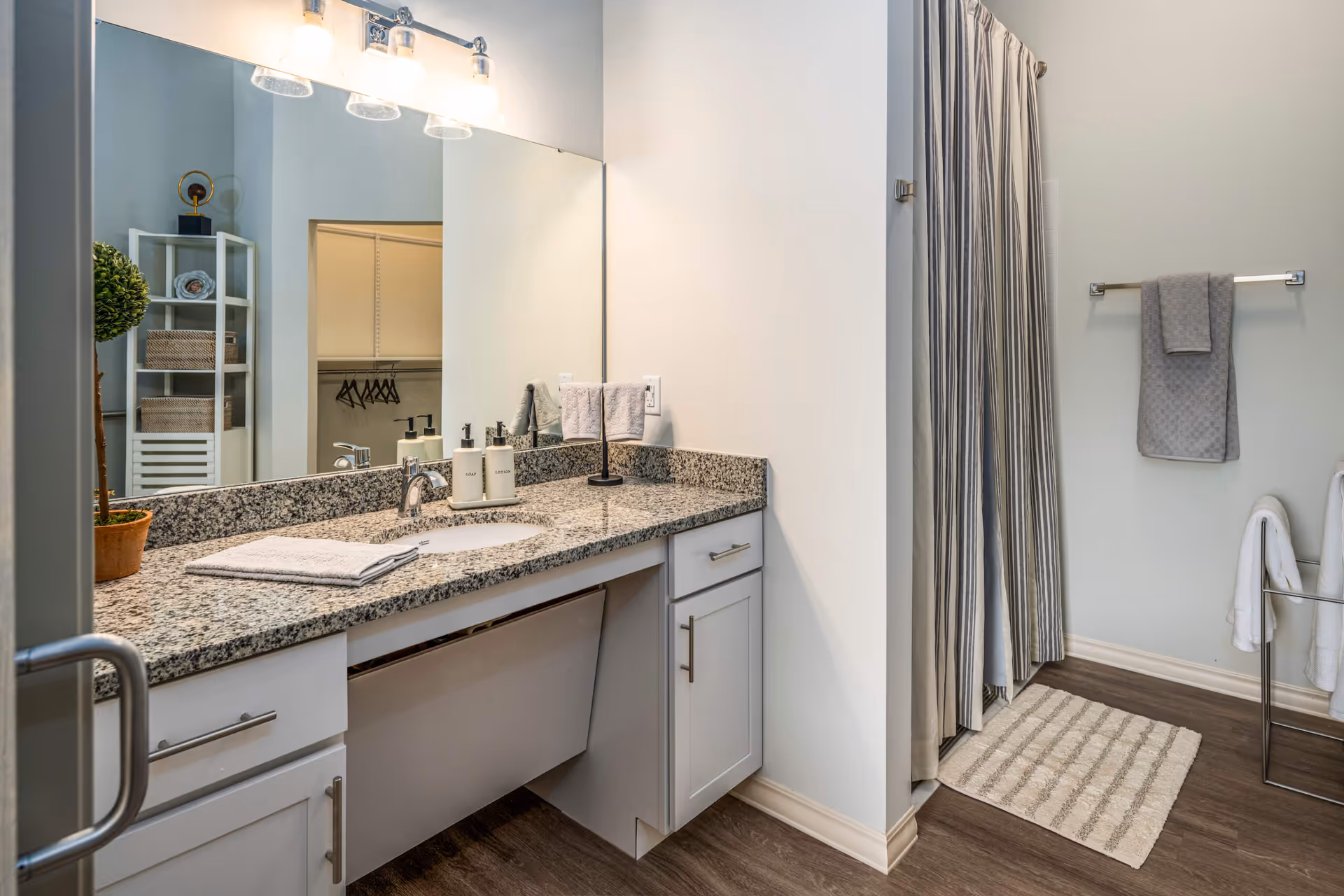 Bright modern bathroom with a granite vanity and sink, large mirror, shower curtain, and towels.