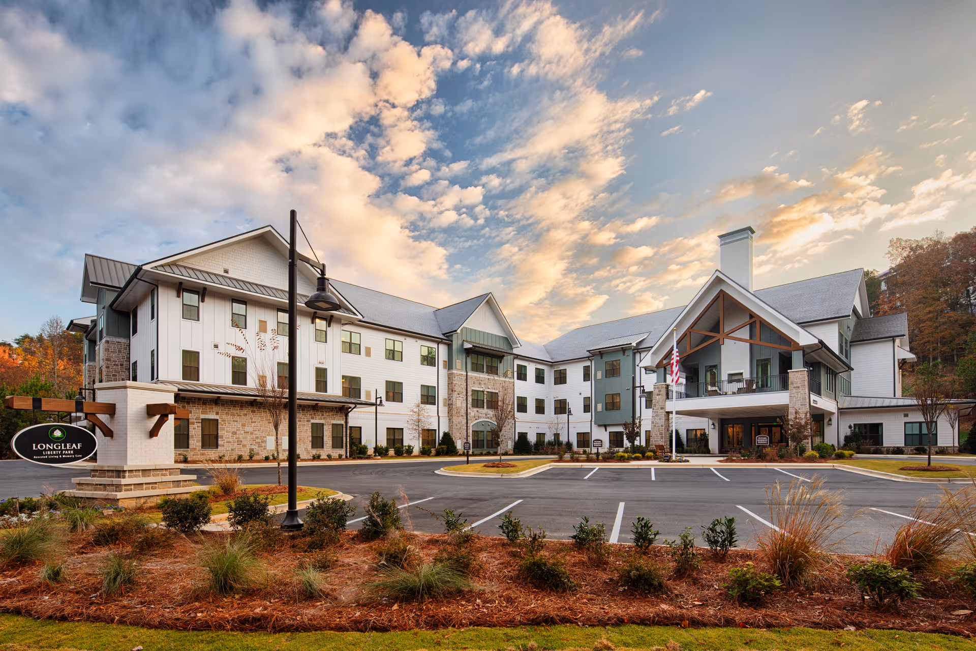 Exterior view of Longleaf Liberty Park senior living facility's multi-story building with a covered entrance, parking lot, and landscaped grounds under a cloudy sky.