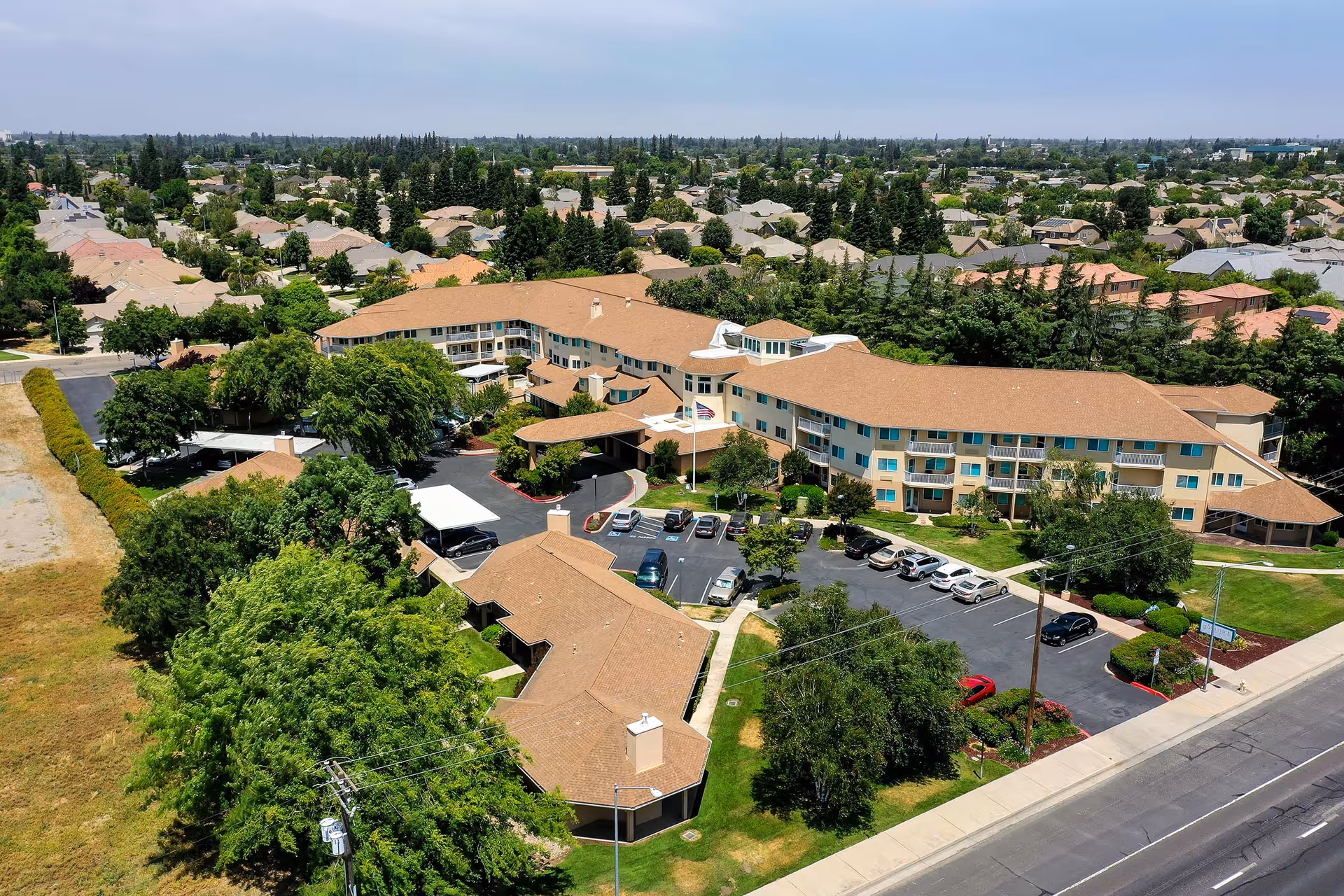 Aerial view of Solstice Senior Living at Lodi showing a large, multi-wing building with tan roofs surrounded by trees and parking lots, located in a suburban neighborhood with many houses and greenery.