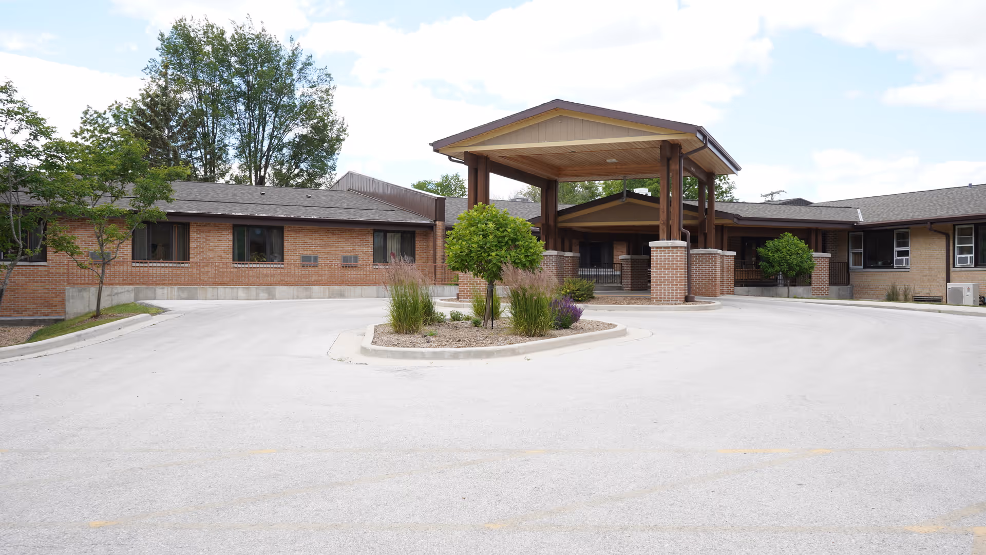Front exterior view of Pine Haven Christian Communities Giddings Avenue Campus showing a single-story brick building with a covered entrance supported by wooden beams and a circular driveway with landscaped greenery in the center.