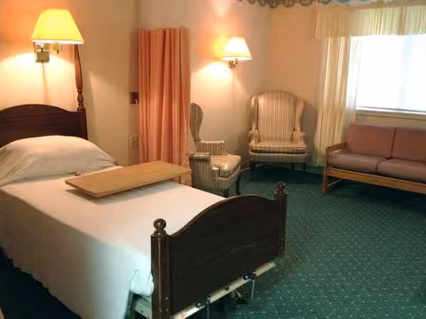 A furnished senior living bedroom with a bed, seating area, and lamps.