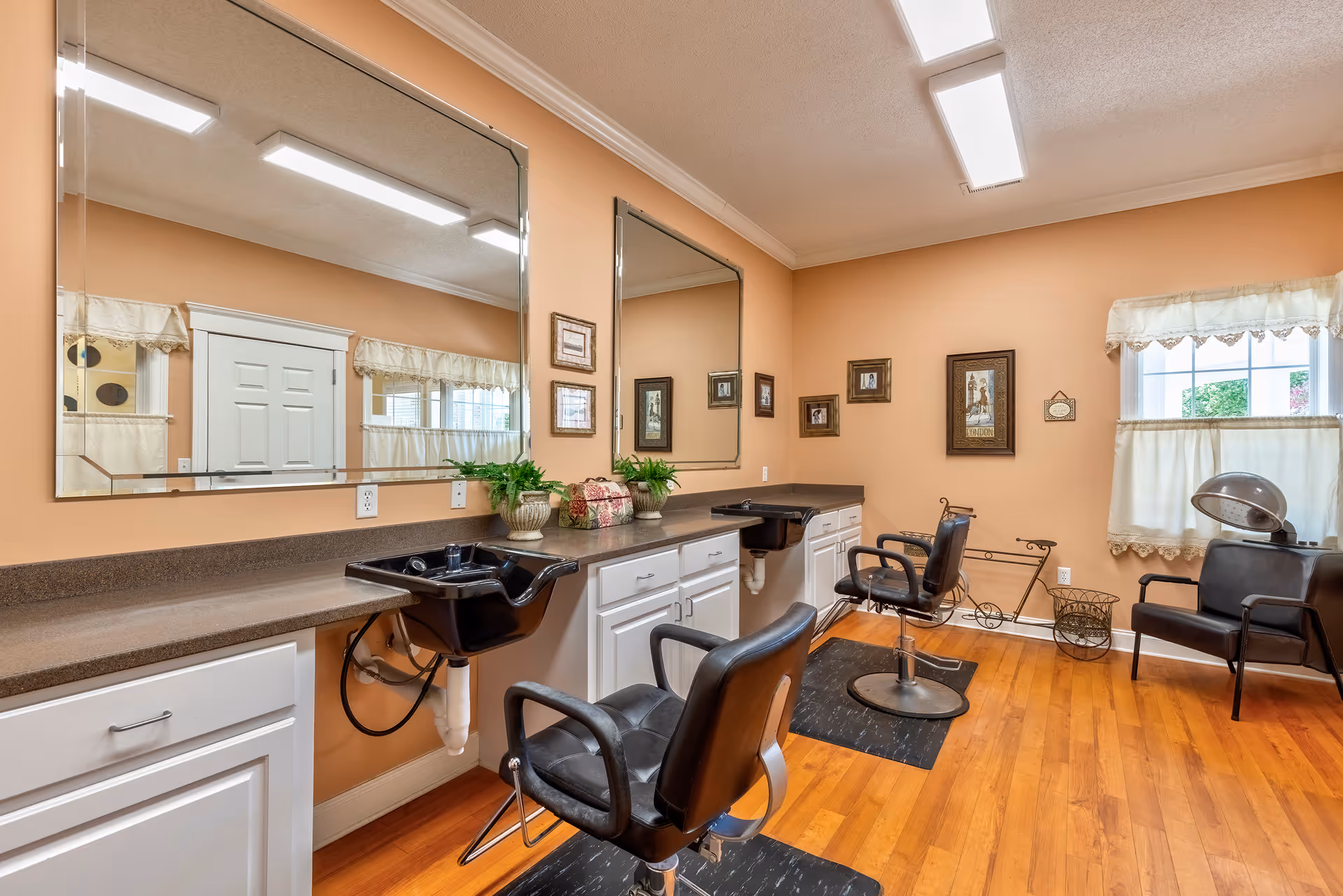 Interior salon/styling room with mirrors, barber chairs, shampoo sinks and wooden floors.