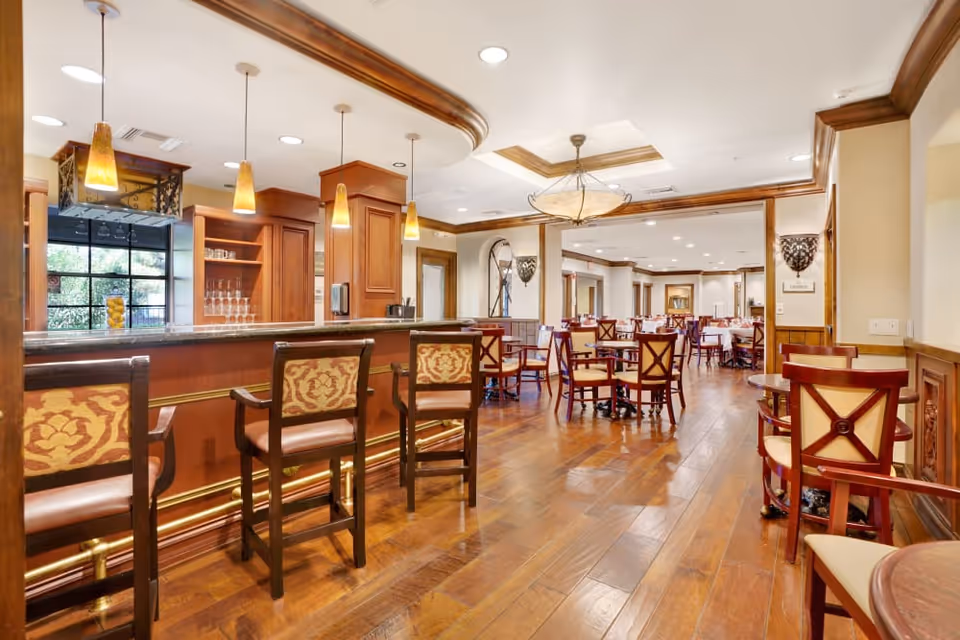 Spacious dining room interior with a wooden bar, pendant lights, and multiple tables and chairs on hardwood floors.