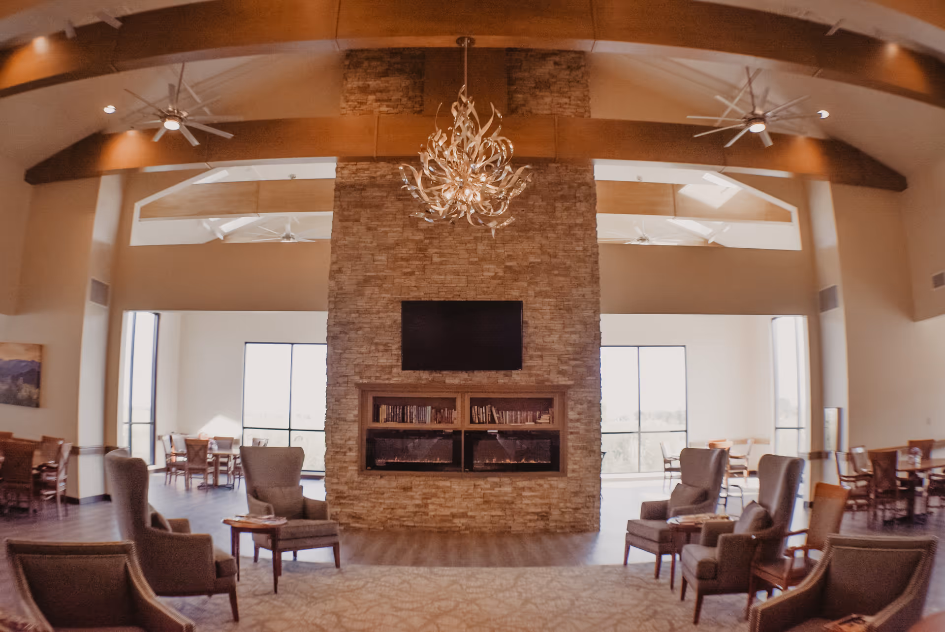 Spacious communal lounge with a central stone fireplace and TV, seating areas and dining tables under high vaulted ceilings.