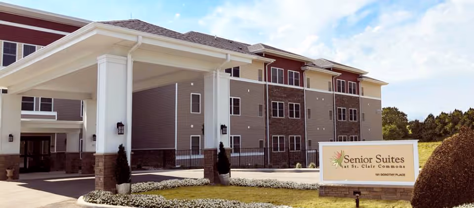 Exterior view of the Senior Suites at St. Clair Commons building showing the covered entrance, landscaping, and a sign.