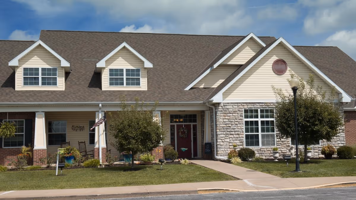 Front exterior of a single-story residential building with a covered porch, dormer windows, and a landscaped lawn.