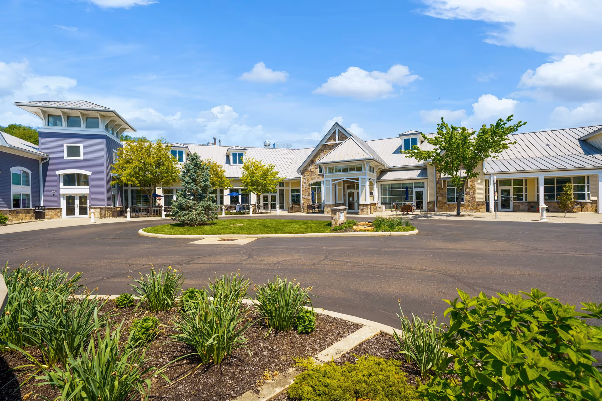 Front exterior of the Otterbein Granville SeniorLife Community building with a circular driveway, landscaped beds, and a blue sky.