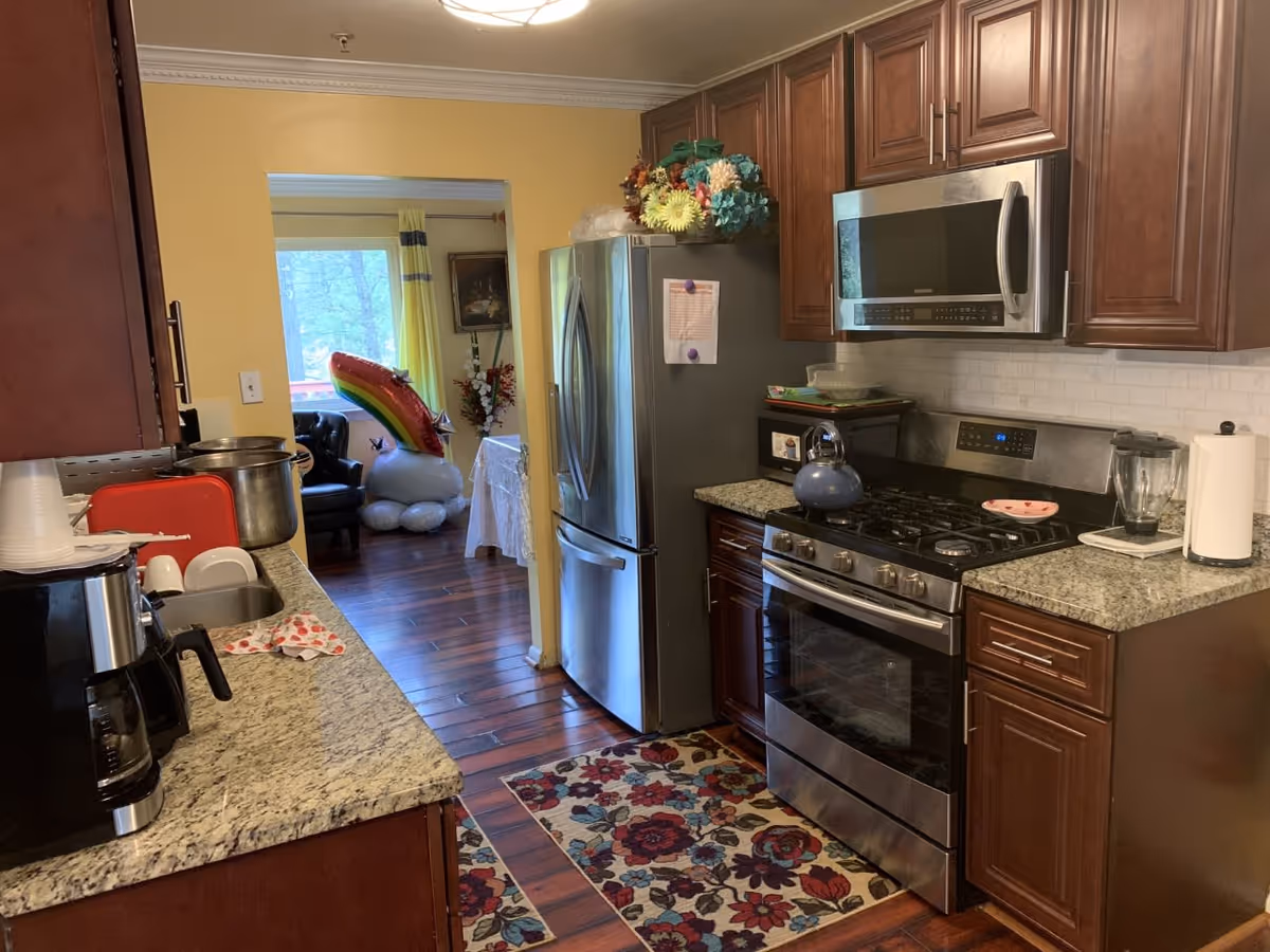 Bright kitchen featuring stainless steel appliances, dark wood cabinets, granite countertops and a floral floor runner, with a view into an adjacent seating area.
