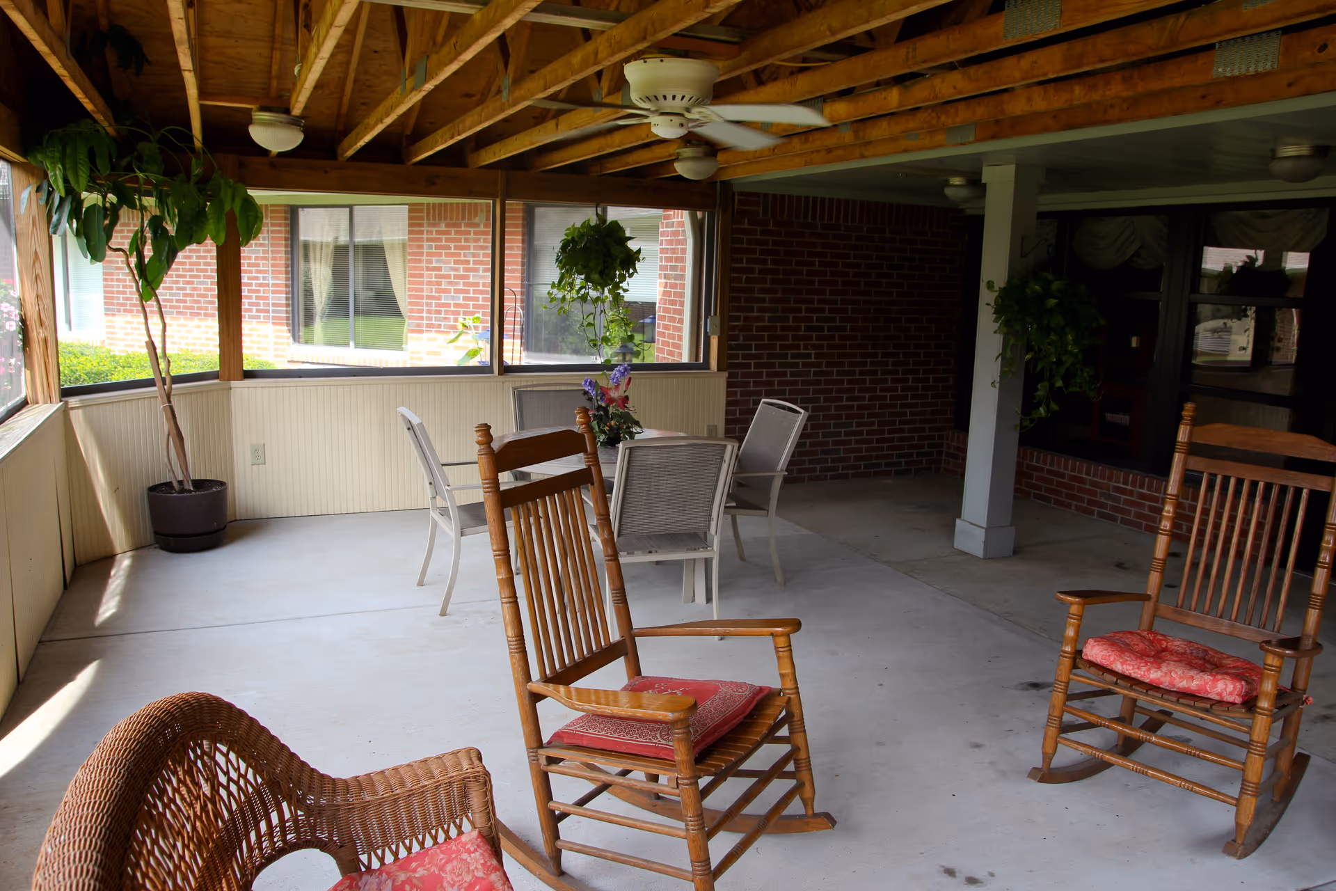 Covered screened patio with rocking chairs, a table and chairs, potted plants and a ceiling fan.