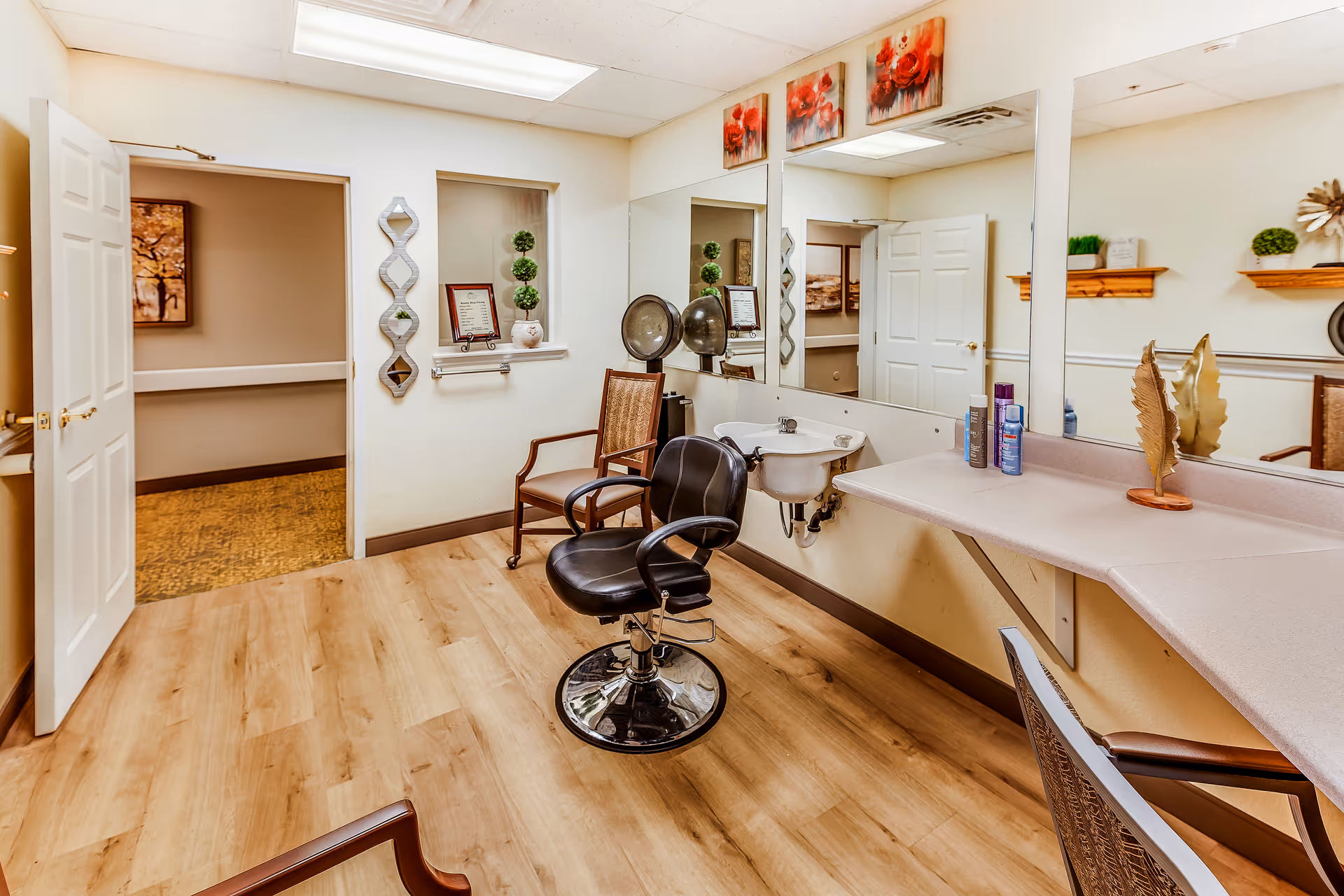 Small hair salon inside a senior living facility with styling chairs, a wash sink, mirrors and a countertop.