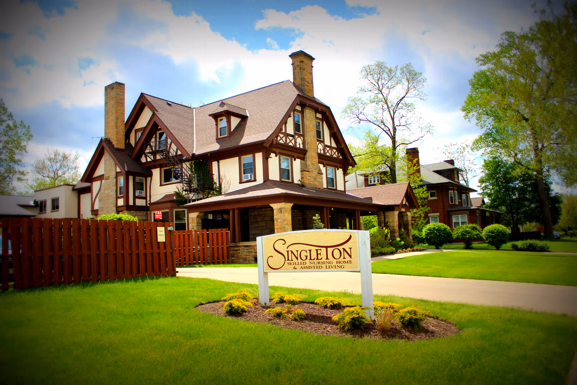 Front view of a large Tudor-style nursing home building with a lawn and a prominent sign reading 'Singleton' in the foreground.