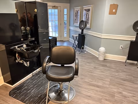 Interior salon area with a styling chair, shampoo sink, hooded hair dryers, and a door leading outside.