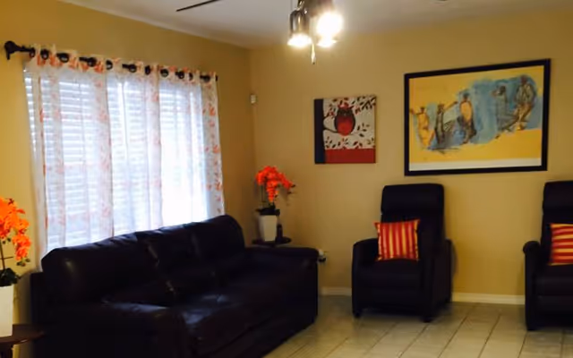 Cozy beige living room with sofa, two armchairs, curtains, artwork, and potted plants.