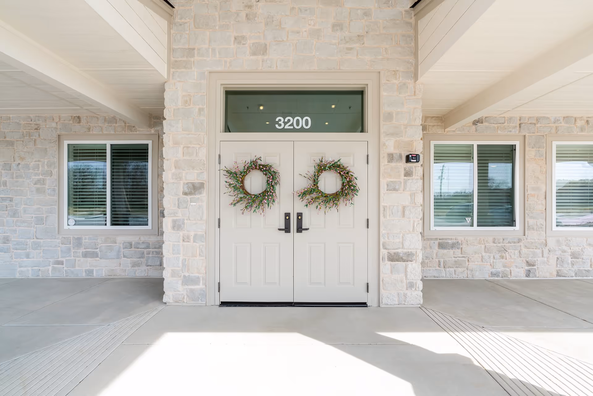 Double front doors of a stone-clad building decorated with wreaths and the number 3200 above them.