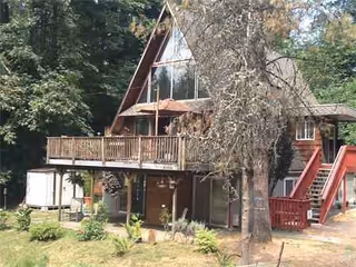 A wooden A-frame senior living building with a deck, stairs, and surrounding trees.