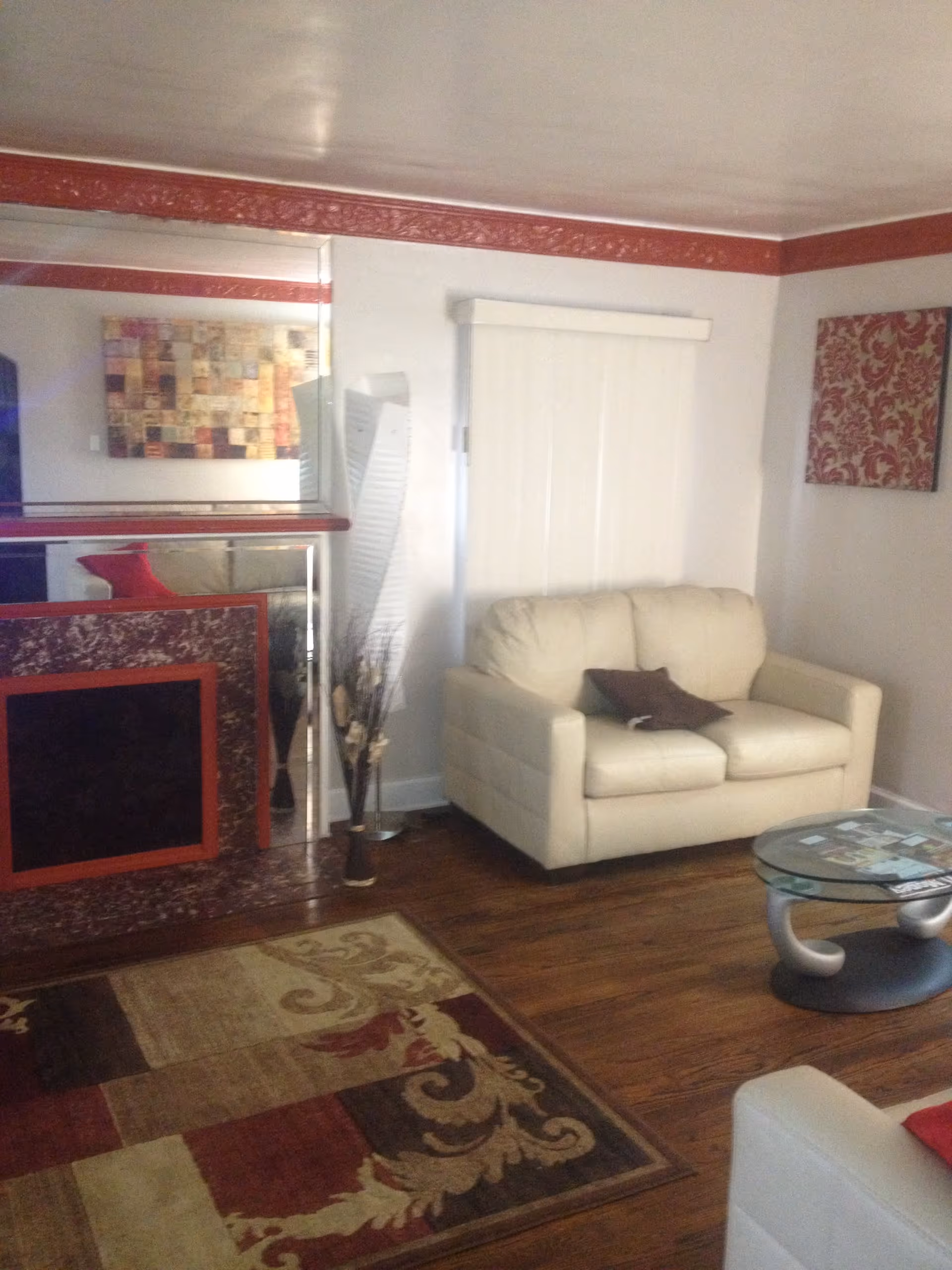 Small living room with a cream loveseat, patterned rug, glass coffee table, and mirrored wall accents.