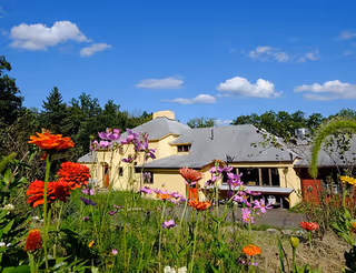 Yellow single-story building with a colorful flower garden in the foreground beneath a bright blue sky.