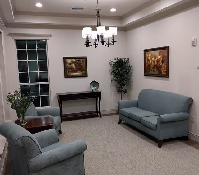 Well-lit sitting room with teal sofa and armchairs, a console table, wall art, a potted plant, and a central chandelier.