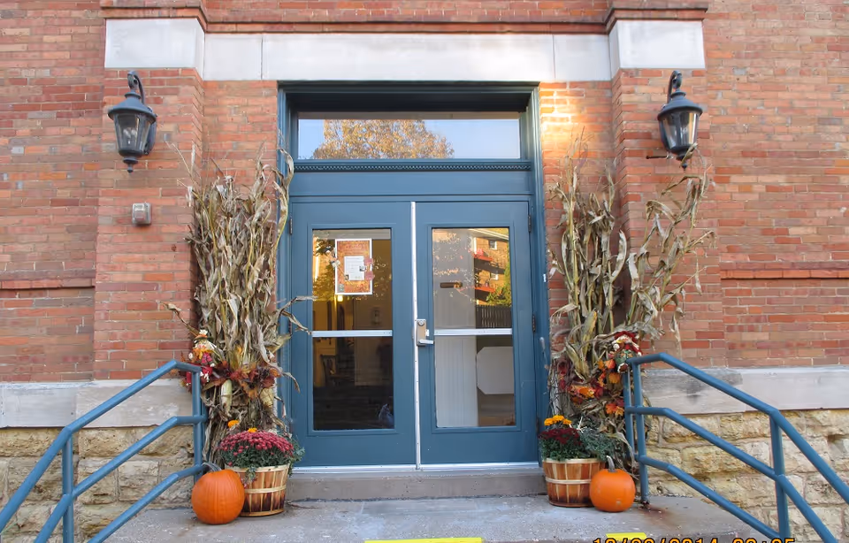 Brick building entrance with blue doors, pumpkins, and autumn cornstalks decorating the front steps.