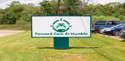 Outdoor scene with a Focused Care at Humble sign on a grassy lot and parked cars.