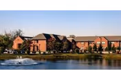 Brick senior living campus by a lake with a fountain and trees.