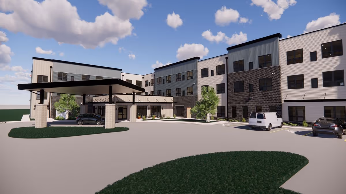 Modern three-story senior living building with a covered drive-up entrance, parked cars, and landscaped islands under a partly cloudy sky.
