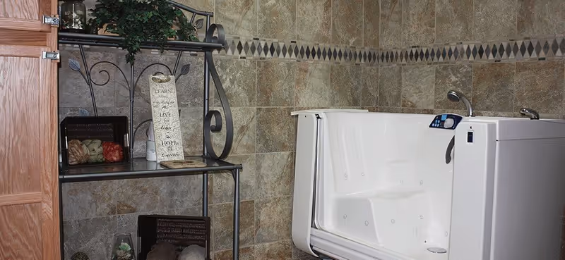 Tiled bathroom with a white walk-in bathtub and a decorative metal shelving unit holding towels and decor.