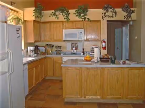 Bright kitchen at Desert Hills Adult Care Home with wooden cabinets, island, and hanging plants.