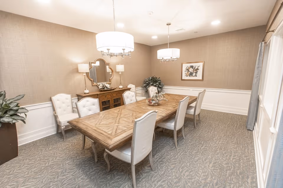 Elegant dining room with a long wooden table, upholstered chairs, chandeliers, sideboard and wall decor.