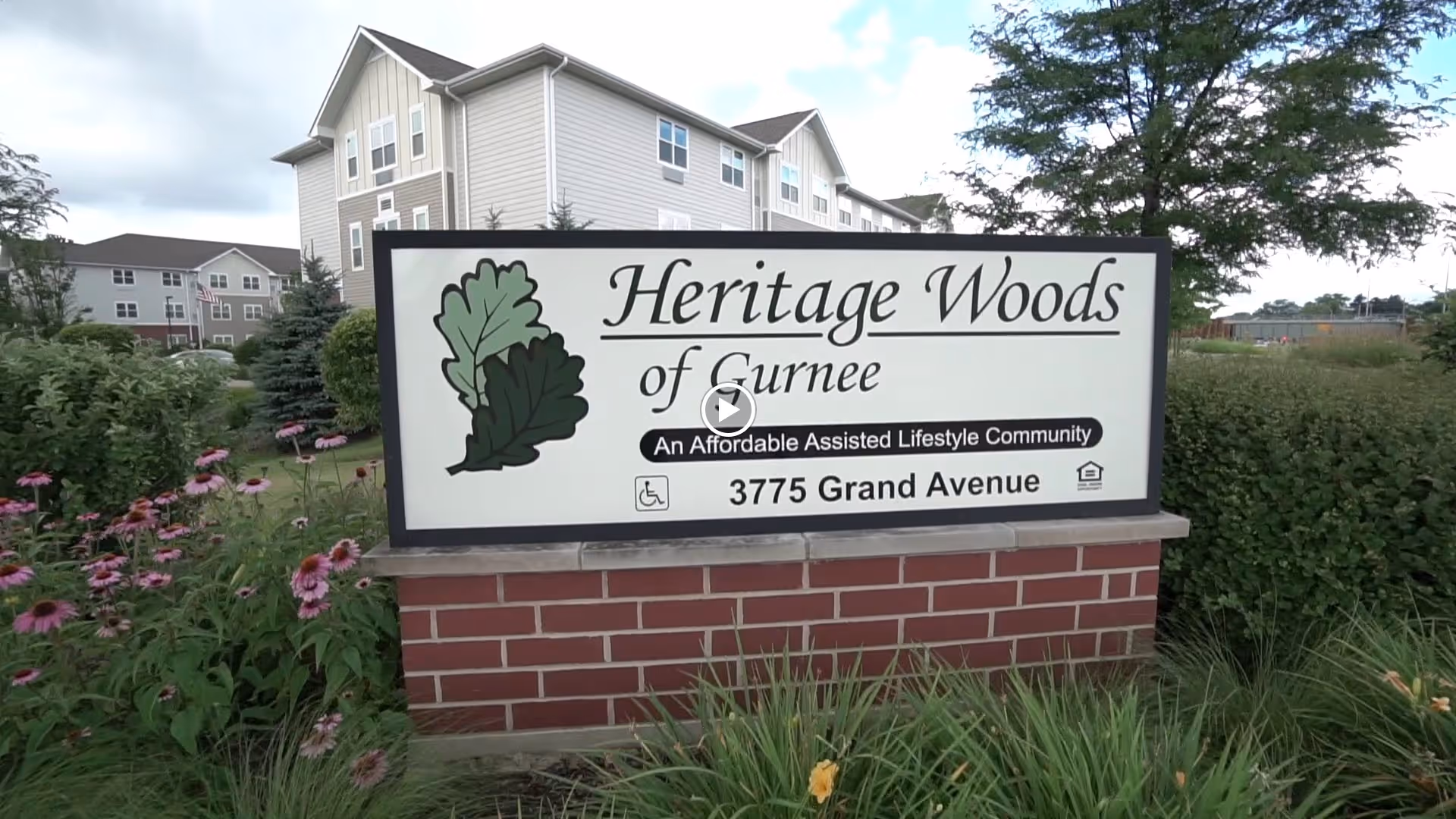 A brick entrance sign reading "Heritage Woods of Gurnee" surrounded by landscaping with the facility building in the background.