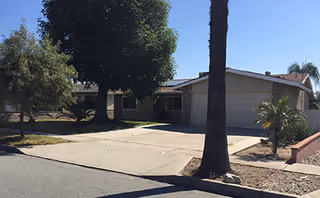 Front exterior of La Fuente Lavender senior living facility with driveway, trees, and palm trees.