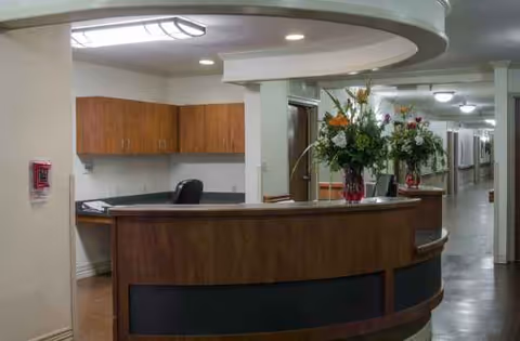 Curved wooden reception desk in a lobby with flowers and a long hallway behind.