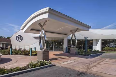 Delmar Gardens on the Green exterior entrance with curved canopy and decorative metal sculpture.